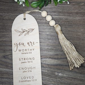 May include: Wooden bookmark with a tassel and a quote that reads "you are - WORTHY romans 5:8 STRONG psalm 18:15 ENOUGH john 3:16 LOVED 2 corinthians 12:19 BEAUTIFUL psalm 139:14"