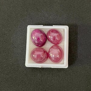 Può includere: Quattro pietre preziose rosa di forma ovale in una scatola bianca. Le pietre preziose sono lisce e brillanti.