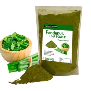 May include: A clear plastic pouch of Natural Lanka Pandanus Leaf Powder with a white label featuring green text, a pile of dark green powder, and images of fresh pandan leaves. Beside it sits a wooden bowl filled with chopped green leaves.