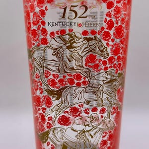 May include: Clear glass featuring a red rose pattern and gold illustrations of horses and jockeys. The text "152 Kentucky Derby" is displayed on the glass. A collectible item for horse racing enthusiasts.