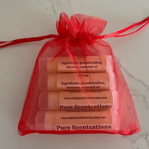 May include: A red mesh bag filled with five small tubes of lip balm. Each tube has a label that reads "Pure Scentsations" and lists the ingredients: grassfed tallow, beeswax, and essential oil. The label also includes the website address www.faithworksbytrina.etsy.com.