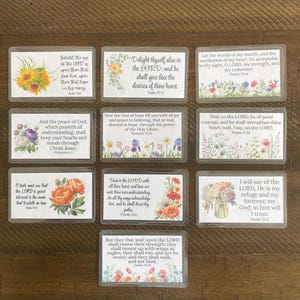 May include: A collection of rectangular cards with floral designs and Bible verses. The cards feature various flower arrangements, including sunflowers, roses, and mixed blooms, with text in a classic font. The overall aesthetic is soft and inspirational.