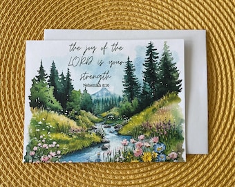 May include: A watercolor greeting card with a landscape scene featuring a river, trees, and flowers. The text "the joy of the LORD is your strength" is written across the top, with "Nehemiah 8:10" below.