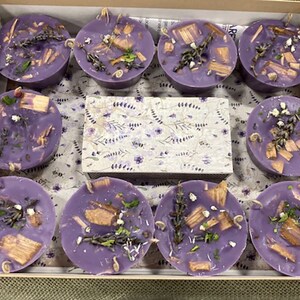 May include: A box of 10 purple scented candles with wood chips and lavender. The candles are in a box with a lavender patterned paper.