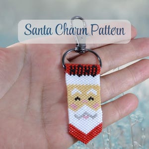 May include: A beaded keyring featuring a Santa Claus design with a red, white, and tan colour palette. The top section displays the text HO HO in black beads. The charm is attached to a dark metal lobster clasp and a circular ring connector.