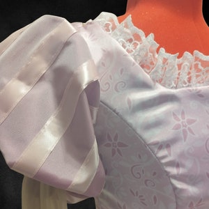 Könnte beinhalten: Ein lavendelfarbenes Kleid mit einem weißen Spitzenkragen und einem Puffärmel mit lavendelfarbenen Satinstreifen. Das Kleid hat ein Blumenmuster.