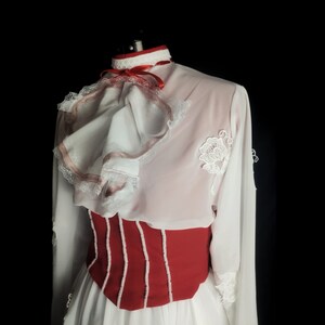 May include: A white blouse with a red and white ruffled collar and a red bodice. The blouse has long sleeves and a white lace trim.