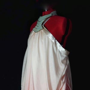 Può includere: Un abito bianco e rosa drappeggiato con un colletto in metallo argentato e turchese.