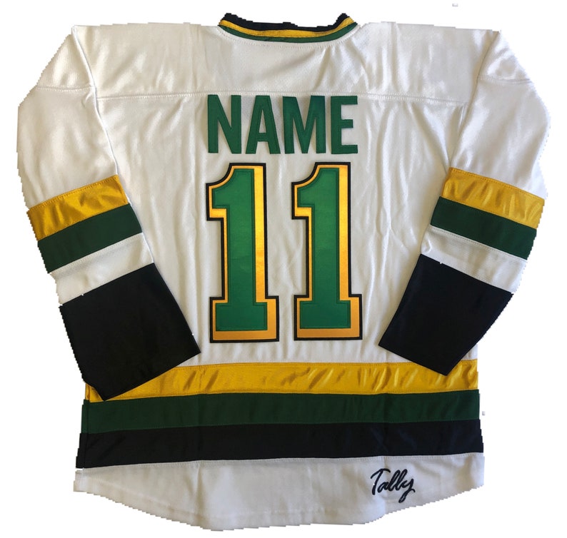May include: White hockey jersey with green and gold stripes. The back of the jersey has the number "11" in gold with a green outline and the word "NAME" above it. The bottom of the jersey has a black stripe with the word "Tally" in cursive.