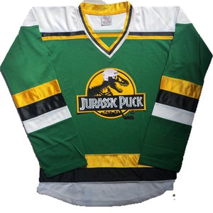 May include: Green and white hockey jersey with a yellow and black stripe pattern. The jersey features a large yellow logo with a dinosaur skeleton and the text "Jurassic Puck".
