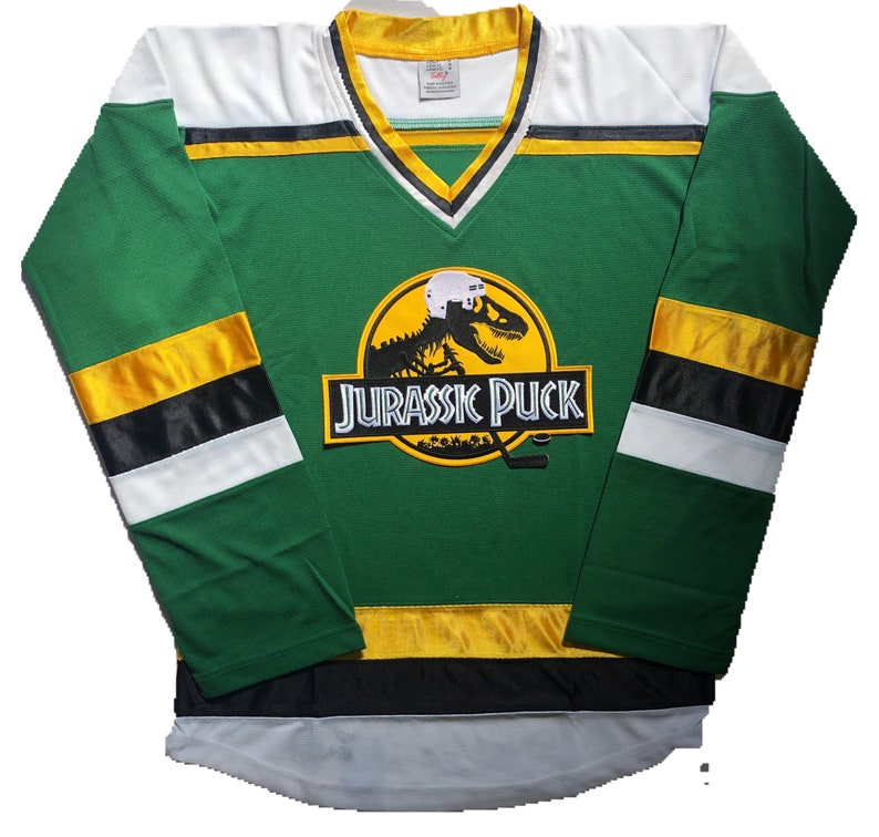 May include: Green and white hockey jersey with a yellow and black stripe pattern. The jersey features a large yellow logo with a dinosaur skeleton and the text "Jurassic Puck".