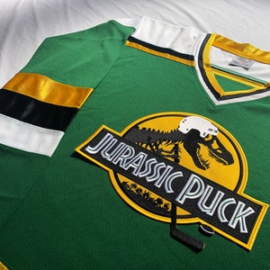 May include: Green and yellow hockey jersey with a dinosaur graphic and the text "Jurassic Puck".