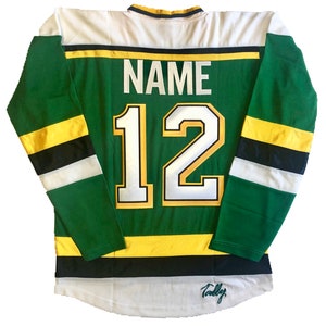 May include: Green and white hockey jersey with black and yellow stripes. The back of the jersey has the number "12" and the word "NAME" above it. The jersey is signed "Tally".
