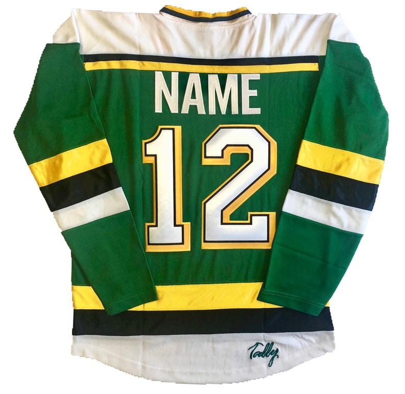 May include: Green and white hockey jersey with black and yellow stripes. The back of the jersey has the number "12" and the word "NAME" above it. The jersey is signed "Tally".