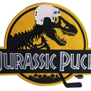 May include: A black and yellow embroidered patch with a dinosaur skeleton wearing a hockey helmet. The text "Jurassic Puck" is below the dinosaur. A hockey stick and puck are at the bottom of the patch.
