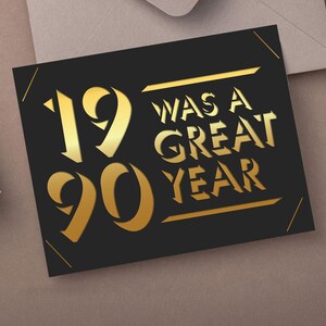May include: A black card with gold lettering that reads "19 was a great year" is displayed. The card is on a neutral surface with a gift and envelope in the background. The numbers "19" and "90" are prominently featured.
