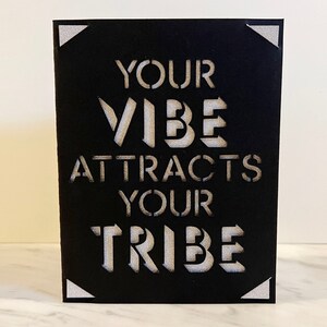 May include: Black card with white cut-out lettering that reads "Your Vibe Attracts Your Tribe".