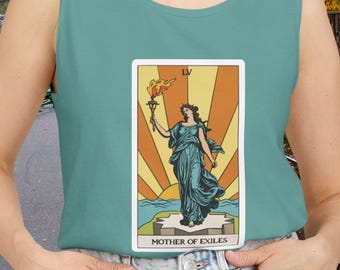 Puede incluir: Camiseta sin mangas turquesa con un diseño de carta del tarot. La carta presenta a una mujer con un vestido turquesa que sostiene una antorcha, con el texto "MOTHER OF EXILES" en la parte inferior. El fondo tiene un diseño de rayos de sol.