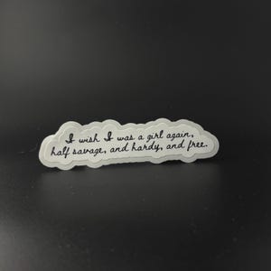 Puede incluir: Una pegatina blanca con el texto "I wish I was a girl again, half savage, and hardy, and free" en cursiva negra. La pegatina tiene forma de nube y est&aacute; sobre un fondo oscuro.