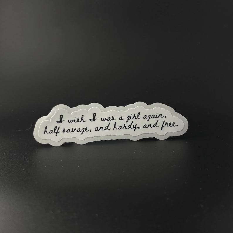 Puede incluir: Una pegatina blanca con el texto "I wish I was a girl again, half savage, and hardy, and free" en cursiva negra. La pegatina tiene forma de nube y est&aacute; sobre un fondo oscuro.