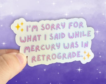 May include: A holographic sticker with the text "I'm sorry for what I said while Mercury was in retrograde." The sticker has a pink and blue iridescent background with yellow stars.