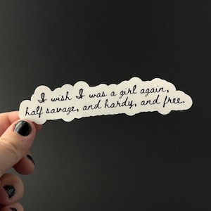 Puede incluir: Una pegatina blanca con un borde en forma de nube y texto negro en cursiva. El texto dice: "I wish I was a girl again, half savage, and hardy, and free."