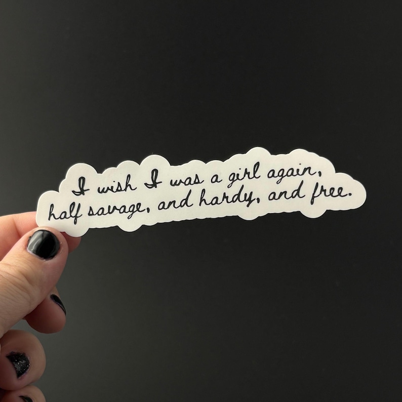 Puede incluir: Una pegatina blanca con un borde en forma de nube y texto negro en cursiva. El texto dice: "I wish I was a girl again, half savage, and hardy, and free."