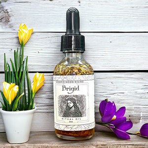 May include: A clear glass bottle with a black dropper top filled with a golden liquid. The bottle has a label that reads "Scorpio Moon Rising" and "Brigid Ritual Oil 2oz". The label also features a black and white illustration of a woman with long hair and a crown.