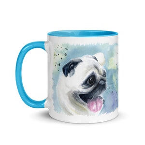 May include: A white ceramic mug with a light blue rim and handle. The mug features a watercolor illustration of a pug with a pink tongue sticking out. The background is a light blue watercolor wash with white and green splatters.