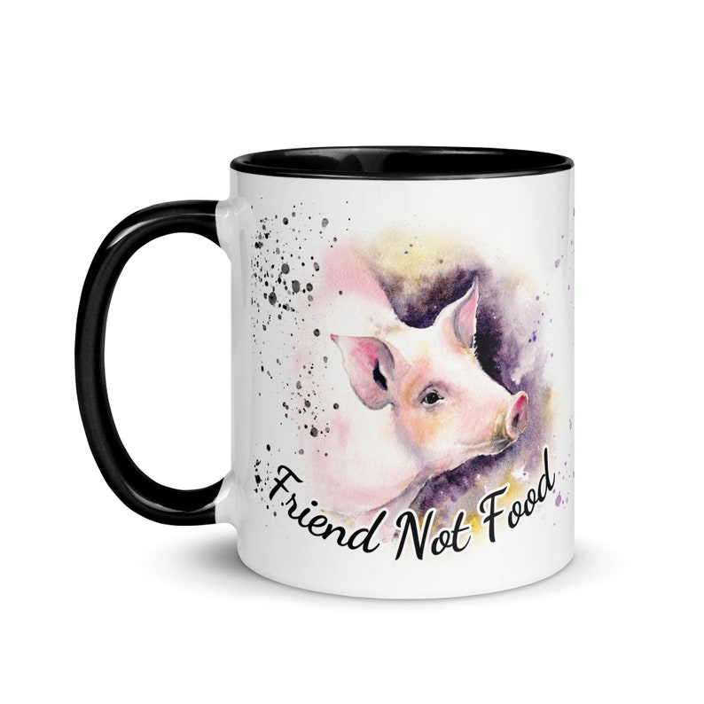 May include: White ceramic mug with a black rim and handle. The mug features a watercolor illustration of a pig with the text "Friend Not Food" in black.