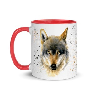 K&ouml;nnte beinhalten: Wei&szlig;e Keramiktasse mit rotem Henkel und Innenraum. Die Tasse zeigt ein Aquarellgem&auml;lde eines Wolfsgesichts mit gelben Augen. Spritzer in Braun und Schwarz akzentuieren das Design.