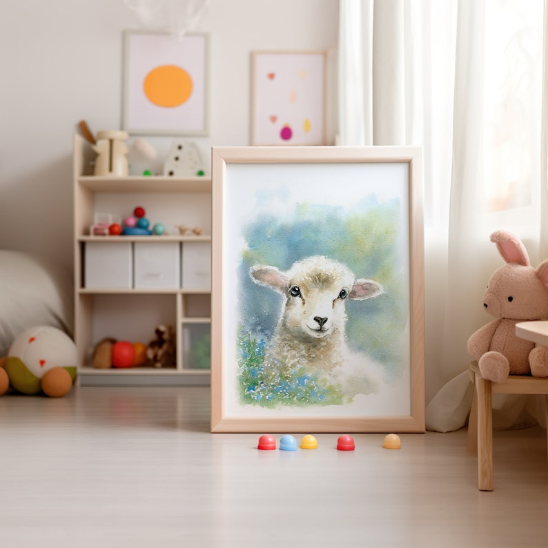 May include: A framed watercolor painting of a white lamb with a blue and green background. The lamb is looking directly at the viewer with its mouth closed. The painting is in a light wood frame and is sitting on a light wood floor.