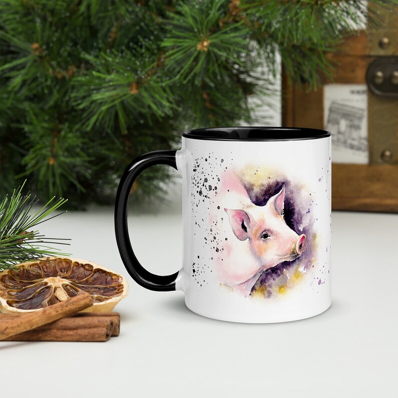 May include: White ceramic mug with a black rim and handle. The mug features a watercolor illustration of a pink pig with purple and yellow accents.