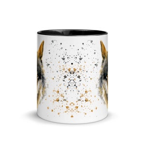 K&ouml;nnte beinhalten: Wei&szlig;er Keramikbecher mit schwarzem Innenraum, verziert mit einer Aquarellillustration eines Wolfsgesichts. Das Design umfasst schwarze und goldfarbene Farbspritzer, die einen einzigartigen, k&uuml;nstlerischen Look erzeugen. Der Becher hat eine Standardgr&ouml;&szlig;e.