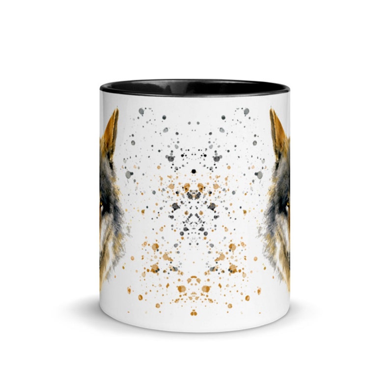K&ouml;nnte beinhalten: Wei&szlig;er Keramikbecher mit schwarzem Innenraum, verziert mit einer Aquarellillustration eines Wolfsgesichts. Das Design umfasst schwarze und goldfarbene Farbspritzer, die einen einzigartigen, k&uuml;nstlerischen Look erzeugen. Der Becher hat eine Standardgr&ouml;&szlig;e.
