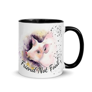 May include: White ceramic mug with a black rim and handle. The mug features a watercolor illustration of a pig's head with the text "Friend Not Food" in black.