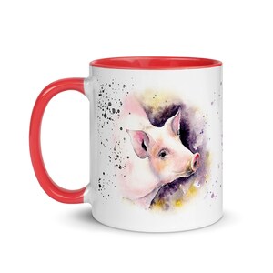 May include: A white ceramic mug with a red rim and handle. The mug features a watercolor illustration of a pink pig with a purple and yellow background.