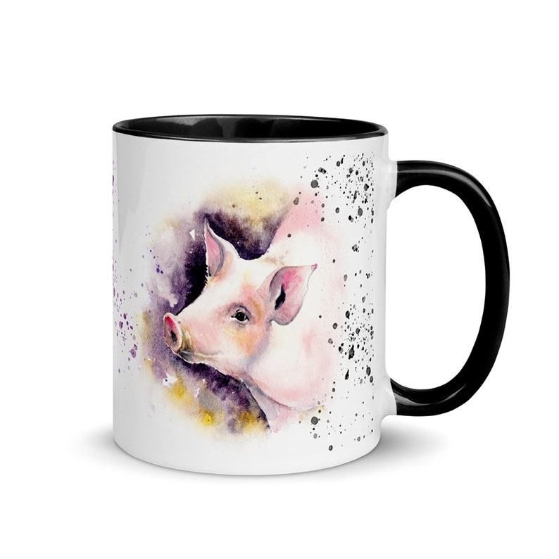May include: White ceramic mug with a black rim and handle. The mug features a watercolor illustration of a pink pig's head with a purple and yellow background.