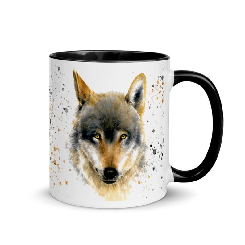 K&ouml;nnte beinhalten: Wei&szlig;e Keramik-Tasse mit einer Aquarell-Illustration eines Wolfs. Der Wolf hat graues und braunes Fell und gelbe Augen. Die Tasse hat einen schwarzen Innenraum und Henkel, mit goldenen und schwarzen Farbspritzern.