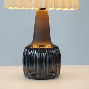 May include: A decorative table lamp with a dark brown ceramic base and a cream-colored lampshade. The base has a textured, geometric design. The lamp is a stylish home decor item.