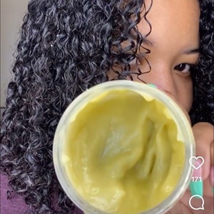 May include: A jar of yellow-green hair product is held up in front of a person's face, with dark, curly hair visible in the background. The text "Reels" is at the top, and the Instagram handle "happycurlss" is shown.