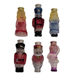 May include: Six vintage glass figurines in the shape of people. The figurines are painted in various colors, including red, blue, and pink. The figurines appear to be from a Christmas ornament set.