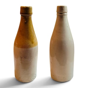 May include: Two ceramic bottles with cylindrical bodies and narrow necks. The left bottle features a two-tone design with a glossy brown upper section and a matte beige lower section. The right bottle is a solid, uniform matte beige color throughout.