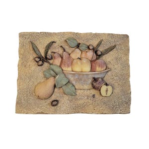 May include: A rectangular, textured wall plaque featuring a relief sculpture of a bowl overflowing with fruit. The fruit includes pears, apples, and olives, in shades of yellow, red, and green. The plaque has a beige background.