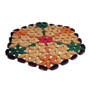 May include: A round trivet made of natural-colored bamboo pieces arranged in a floral pattern. The flowers are accented with green, orange, and red petals. The trivet's edge is a dark purple color. This decorative item is designed to protect surfaces from heat.