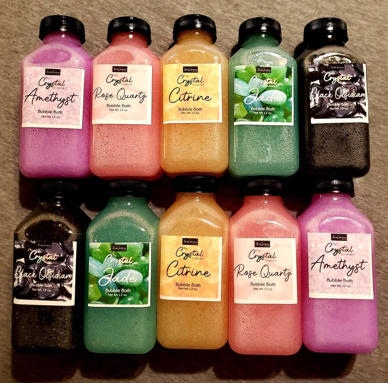 May include: Ten 12-ounce bottles of bubble bath, each with a different crystal theme. The bottles are clear and have a textured surface. The labels are white with black text and feature a crystal image. The crystals are amethyst, rose quartz, citrine, jade, and black obsidian.