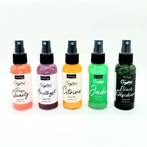 May include: Five 2-ounce bottles of body mist with different crystal-themed scents: Rose Quartz, Amethyst, Citrine, Jade, and Black Obsidian. Each bottle has a black spray nozzle and a label with the crystal name and "Body Mist" printed on it.