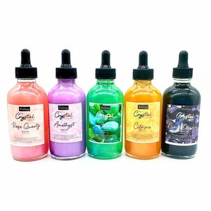 May include: Five glass bottles of body oil with dropper tops. The bottles are labeled with the text "The Crystal Collection" and the names of different crystals: Rose Quartz, Amethyst, Jade, Citrine, and Black Obsidian.