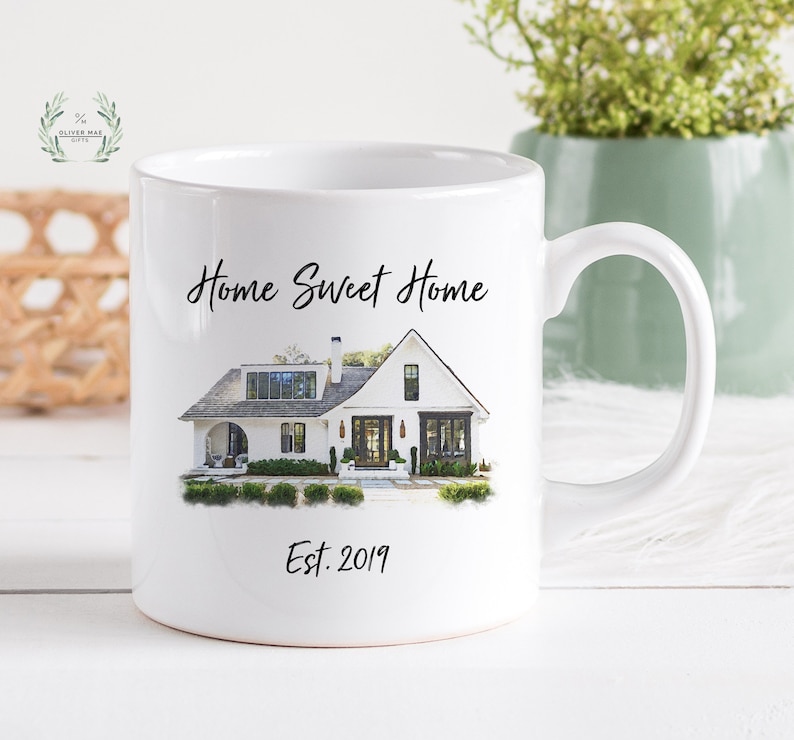 May include: White ceramic mug with a watercolor illustration of a white house with black windows and a black door. The text "Home Sweet Home" is printed above the house and "Est. 2019" is printed below the house.
