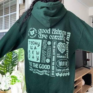 May include: Green hooded sweatshirt with a variety of positive affirmations printed on the back, including "good things are coming", "stay positive", "happy days ahead", "today is a new day", "see the good", "you are exactly where you need to be", "you're doing great", "just be yourself", "you got this", and "know your worth".